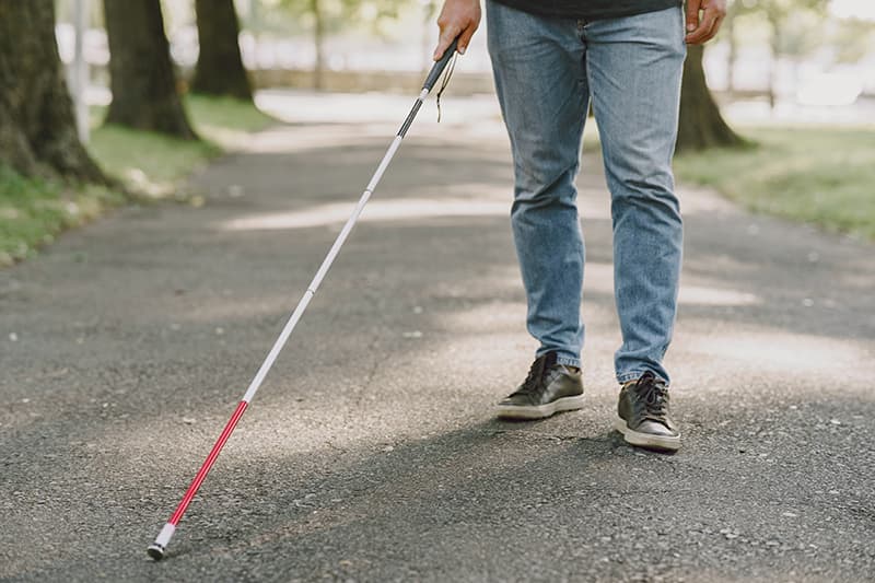 foto de un chico ciego con bastón paseando por parques, con tejanos y zapatillas deportivas